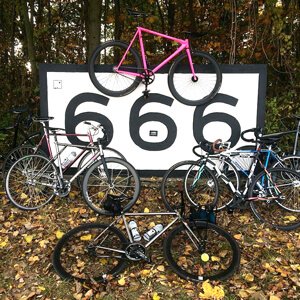 Multiple fixed gear bikes standing around a big sign with 666 written on it